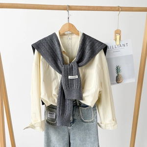 Detail view of dark grey knitted shawl with embroidered logo and beige shirt on a hanger