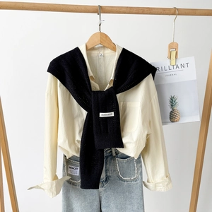Detail of a minimalist black knit shawl with BONOGEED label over a beige shirt and pearl jeans