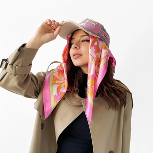 Detail of floral satin scarf styled with a pink baseball cap and khaki trench coat