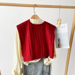 Detail of red knitted shawl vest with textured vertical stripes layered on a beige shirt