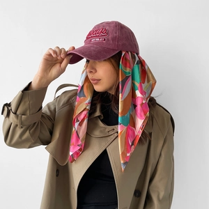 Close-up of a burgundy vintage baseball cap paired with a vibrant printed silk neck scarf
