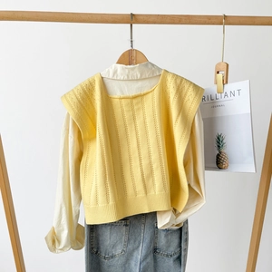 Detail view of a yellow knitted vest with vertical textures on a wooden hanger