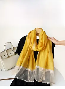 Détail d'un châle en soie jaune avec patchwork en maille et décorations de perles blanches