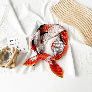 Detail of pleated orange and cream satin scarf with floral patterns on a wooden tray