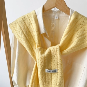 Detail showing knit texture and brand label on a light yellow shawl over a shirt
