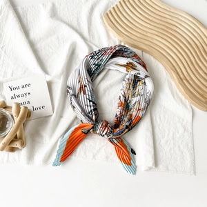 Detail of pleated silk scarf featuring tropical orange floral and bird prints on wood tray