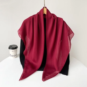 Detail of burgundy chiffon scarf draped over black knitwear with sheer texture
