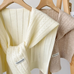 Detail of hollow knit shawl featuring pointelle texture and ribbed hem on wooden hangers