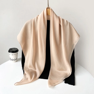 Detail of champagne semi-transparent silk scarf draped on a wooden hanger showing fabric texture