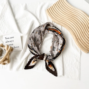 Detailed close-up of pleated satin scarf with abstract floral patterns on wooden tray