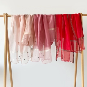 Détail de foulards légers roses et rouges avec bordure dorée et finitions en perles