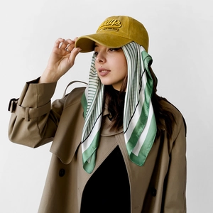 Detail of satin square scarf with green stripes styled on a mustard baseball cap