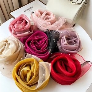 Détail de foulards en soie et laine avec perles, pliés en roses sur une table blanche