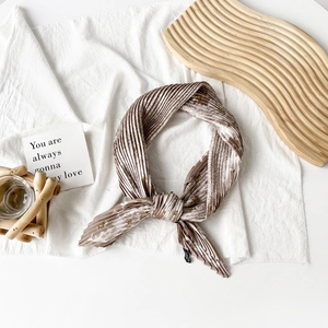 Detail of floral printed pleated silk scarf in earth tones on a rustic wooden tray