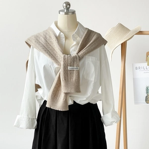 Detail of beige knit shawl texture with woven brand tag over a white shirt