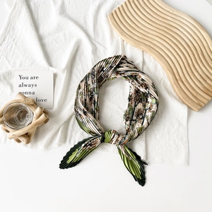 Detail of pleated silk scarf with green floral print on a natural wooden display