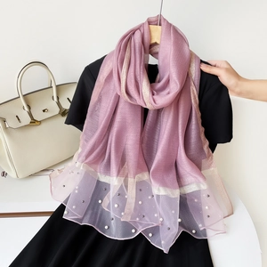 Détail d'une écharpe violette avec rayures dorées, perles et bordures à volants