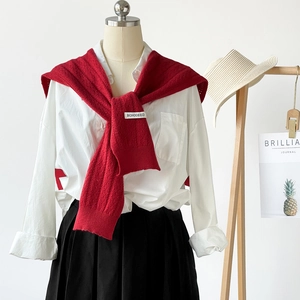 Detail view of a white shirt layered with a red knit shawl and black pleated skirt