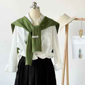 Detail of a grass green knit shawl over a white shirt with an elegant woven brand tag