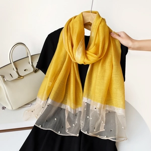 Détail d'une écharpe en soie jaune avec bordure pailletée argentée et perles