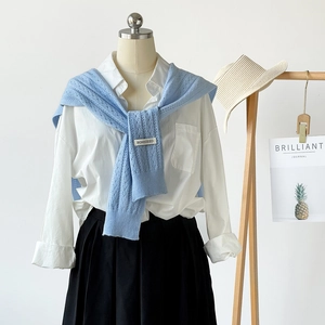 Detail view of light blue hollow knit shawl with brand label on white shirt