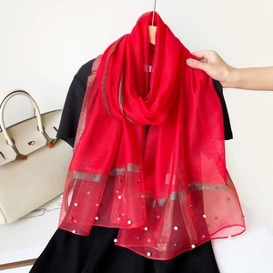 Détail d'un châle en soie rouge avec liseré doré et ornements de perles élégantes