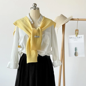 Detail of pale yellow knitted shawl over white shirt with black skirt on a mannequin