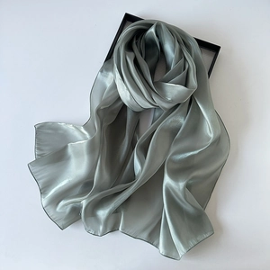 Close-up of sage green organza silk scarf with glossy texture on a gift box