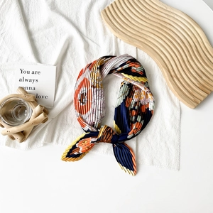 Detailed close-up of pleated satin scarf with floral patterns on a wooden tray