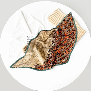 Detailed view of pleated silk scarf with orange maple leaf print on beige satin fabric
