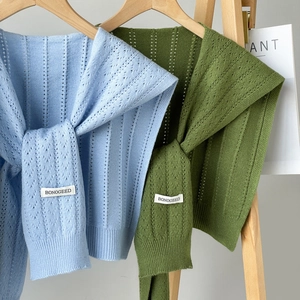 Knitted hollow shawl in light blue and olive green colors on a wooden hanger