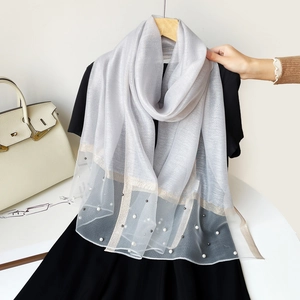 Détail d'une écharpe gris clair semi-transparente avec perles et fils de soie dorés