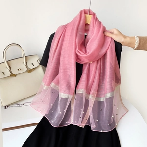 Détail d'une écharpe en soie rose avec ourlet en tulle violet et ornements de perles