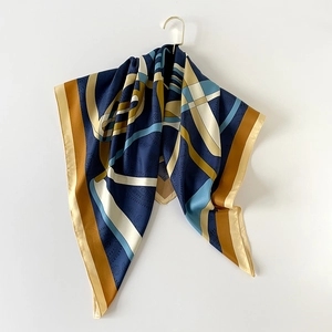 Elegante sciarpa in seta con stampa geometrica blu e caramello appesa su sfondo bianco