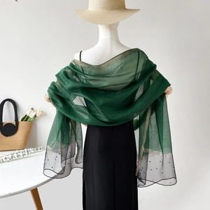 Détail de châle vert foncé avec bordure dorée, perles et ourlet en tulle sur mannequin