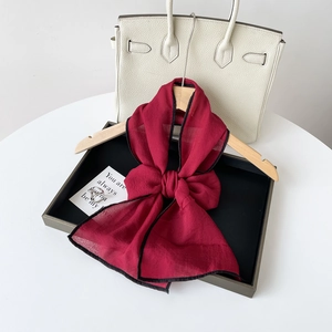 Λεπτομέρεια από μπορντό μεταξωτό φουλάρι με μαύρο σιρίτι δεμένο σε φιόγκο σε κρεμάστρα