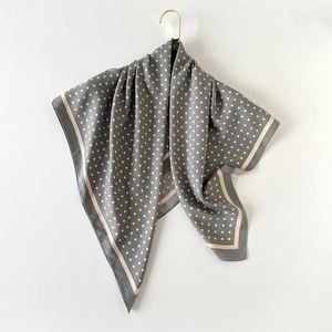 Foulard en soie grise à pois avec bordure crème suspendu sur un fond blanc épuré