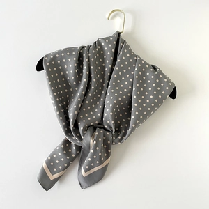 Détail d'un foulard en soie gris à pois beige suspendu sur un cintre noir élégant