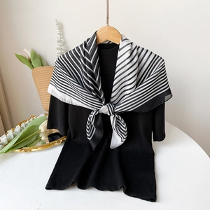 Detail of a thin black and white striped silk scarf knotted on a black knit top