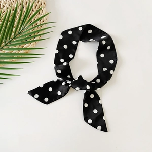 Detailed view of polka dot silk skinny scarf tied in a knot on a woven mat