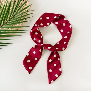 Close-up of a burgundy polka dot silk scarf tied in a bow on a summer resort background