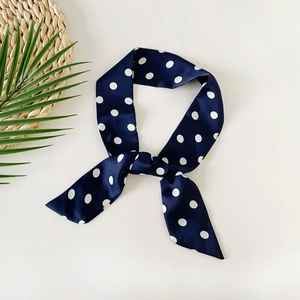 Detail shot of navy blue polka dot silk scarf tied in a bow on a flat lay background