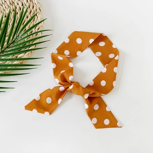 Close-up of orange polka dot skinny silk scarf with diagonal cut ends on a white desk