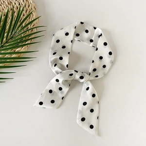 Detail of white polka dot silk scarf tied in a bow with soft fabric texture and glossy finish
