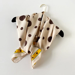 Détail d'un foulard en soie à pois café beige avec un drapé élégant sur un cintre