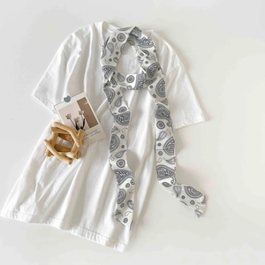 Detailed close-up of a long narrow white silk scarf featuring black paisley patterns