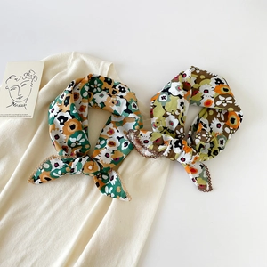 Detailed view of two cotton floral scarves with zig-zag stitched edges on beige fabric