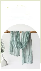 Detailed texture of sage green crinkled jersey scarf hanging on a wooden branch