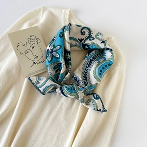 Detail of blue paisley cotton scarf tied elegantly on a beige knit sweater collar