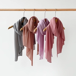 Detail of elegant pleated scarves in grey, soft pink and lilac hanging on wooden hangers